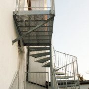 external platform with angle brace against a white building and a spiral staircase