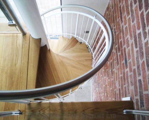oak steps on a spiral stair with a red brick wall to side