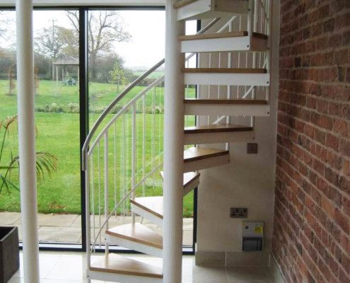 white steel spiral staircase in front of double glass door with garden beyond