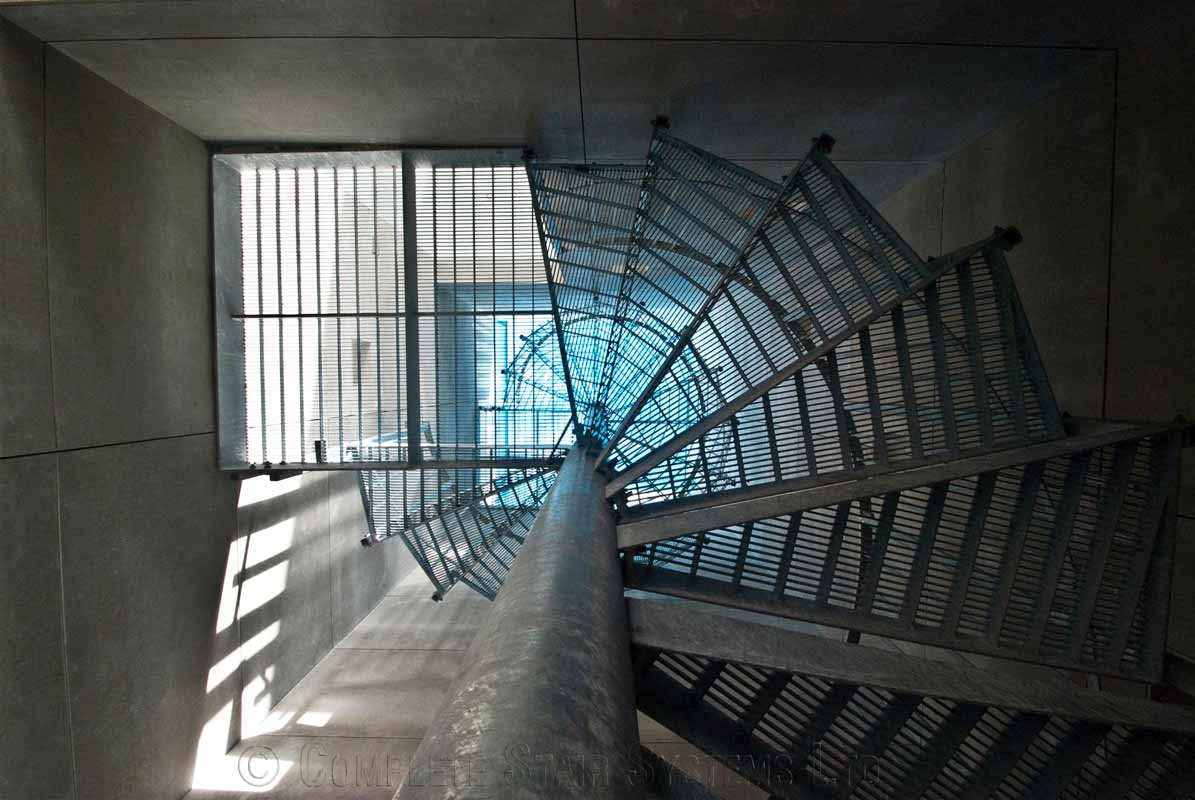 Bespoke Spiral Staircase Farnham - Steel Spiral - 1 looking up through the perforated steps of a spiral staircase