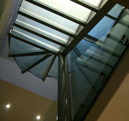 looking up at a glass step spiral staircase with a glass infill panel