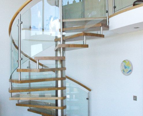 glass panels to the side of a spiral staircase with oak steps in a house
