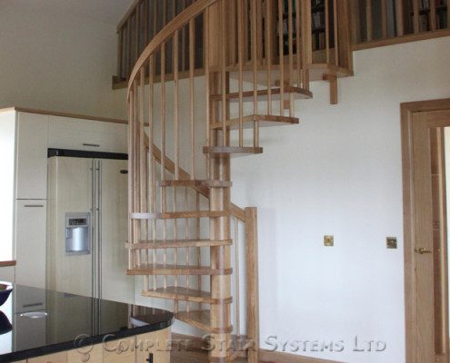 wooden spiral stair leading to a mezzanine floor above a kitchen
