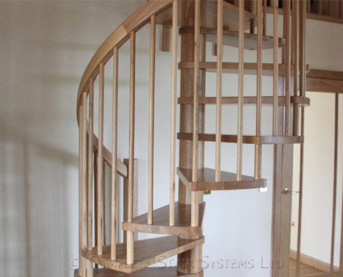 wooden spiral staircase with a white wall behind