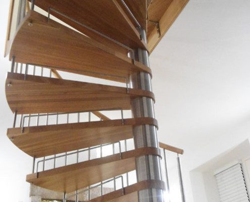 looking up at an oak spiral stair in a living rom with a wood fire