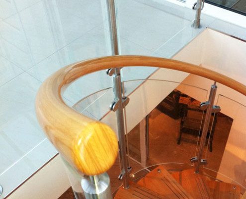 close up of timber handrail on a spiral staircase alongside glass panels