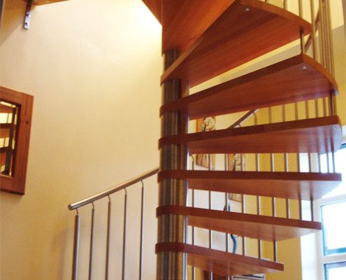 light wood spiral staircase with open risers and a stainless steel handrail
