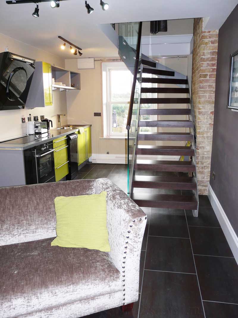 Bespoke Staircase Kent - Model 500 sofa in front of a model dark wood and steel stair and kitchen behind