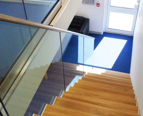 Bespoke Staircase Romsey - Model 500 oak staircase with glass side on a stair in an office with blue carpet