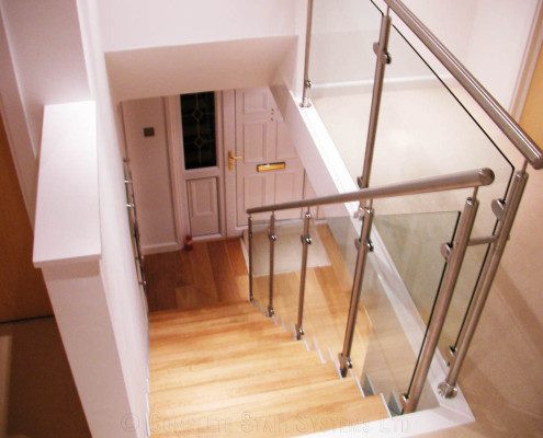 stainless steel handrail at the top of a glass and wood stair in a house