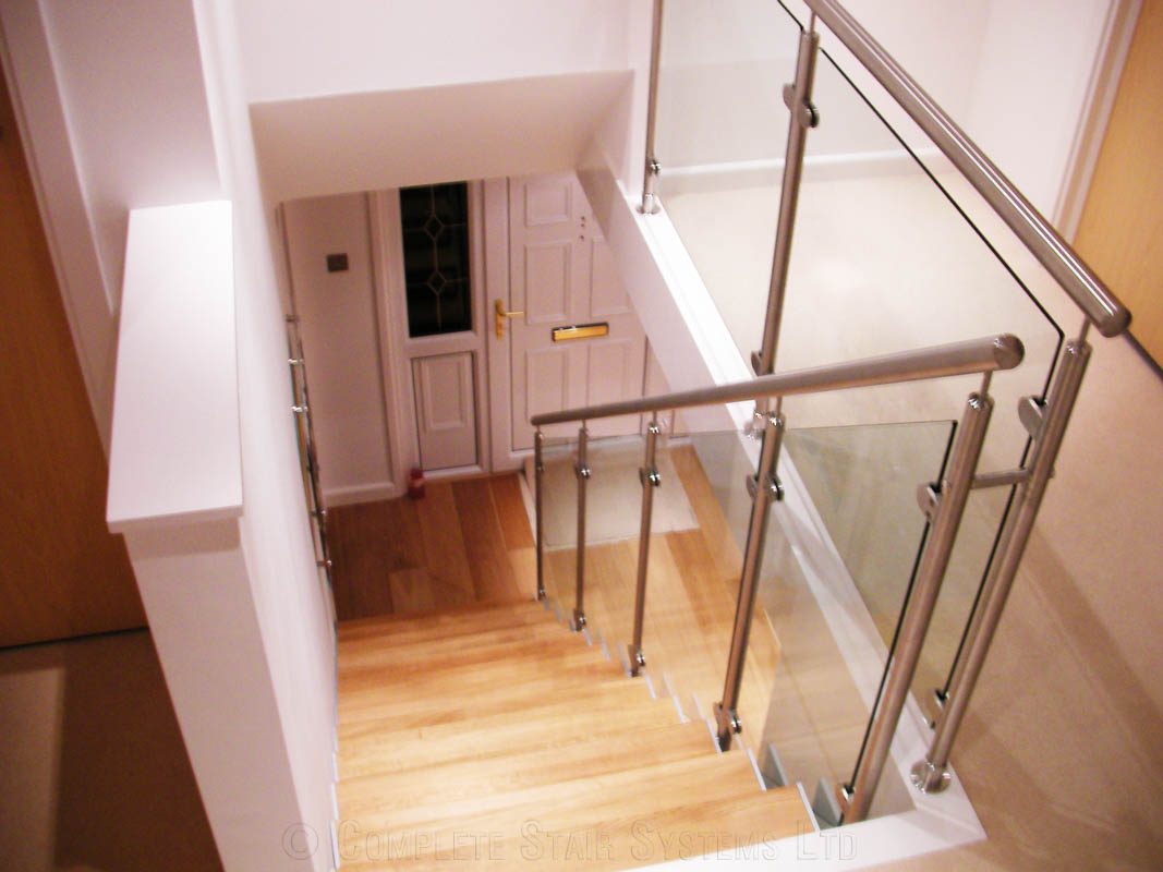 stainless steel handrail at the top of a glass and wood stair in a house