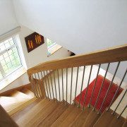 looking down a oak staircase with red rug on floor below