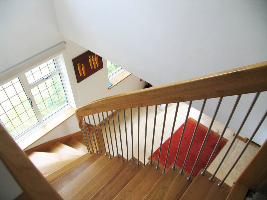looking down a oak staircase with red rug on floor below