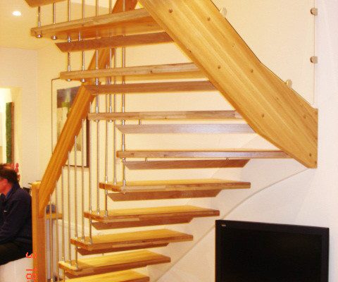 television below an open riser oak staircase with glass infill panel