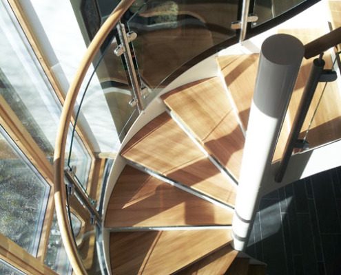 oak treads on a spiral staircase in front of a window with glass panels wrapping around the spiral staircase