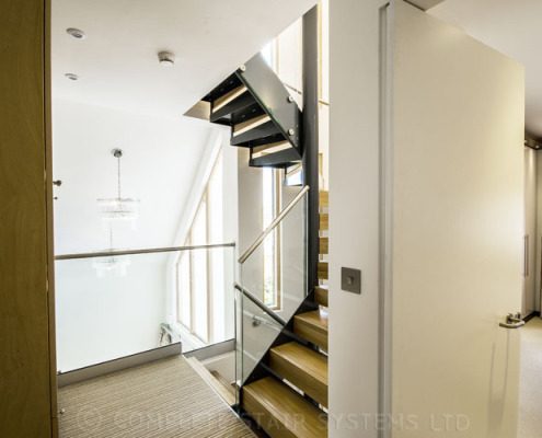 mid landing of a spiral staircase with oak steps and frameless glass balustrade