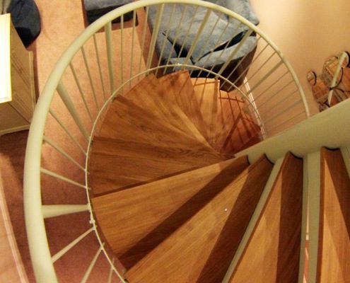 oak treads on a white steel spiral staircase with blue sofa behind