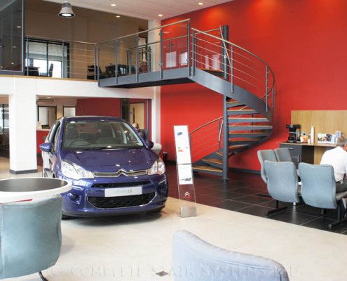car showroom with grey spiral staircase with red wall behind