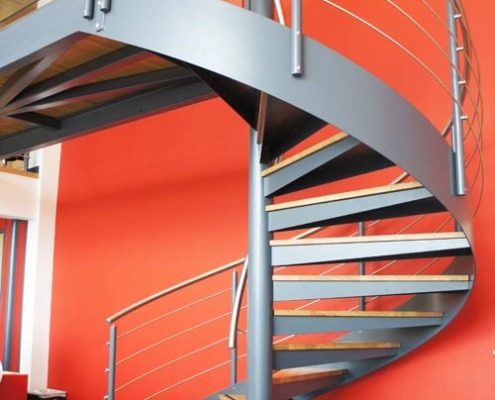 double height red wall behind a grey steel spiral staircase