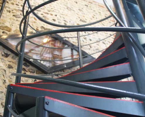 black steps on a spiral stair with a stone wall behind