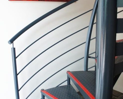 bottom steps of a black spiral staircase with grey carpet below