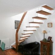 open and light stair in a dining room next to a dining table with green chairs