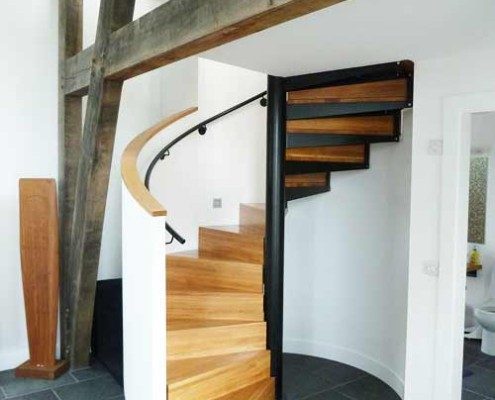 curved white wall behind an oak spiral staircase in timber framed building