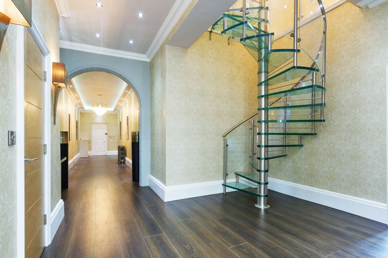 Glass balustrade wrapping around a glass tread spiral stair in a hallway