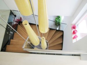 looking down in to a stairwell containing a oak tread staircase in a half turn with glass balustrade