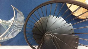 two spiral staircases in a stair showroom , one with glass steps and one with black steps
