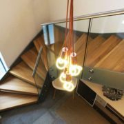 suspended lights next to steel and wooden staircase with glass panels