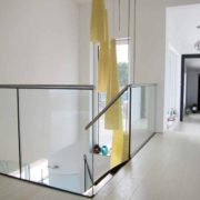landing with large yellow suspended light down a stairwell with frameless glass around
