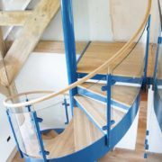 blue spiral stair with curved glass panels with oak handrail