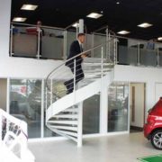 man walking up a white steel spiral staircase in a car showroom