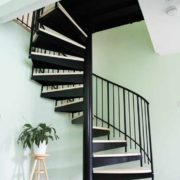 light green wall behind a black spiral staircase and grey timber floor