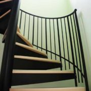green wall behind part of timber stepped black steel spiral stair