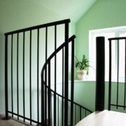 green wall behind a spiral staircase with black balustrade and wooden steps