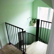 square top platform of spiral staircase with black spindles with green room behind