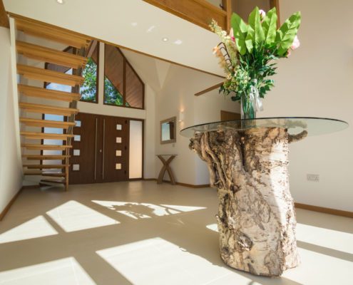 Wood and glass table on polished floor in hallway with floating stair beyond