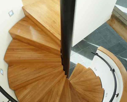 looking down on the oak steps of a spiral staircase with black wall mounted handrail