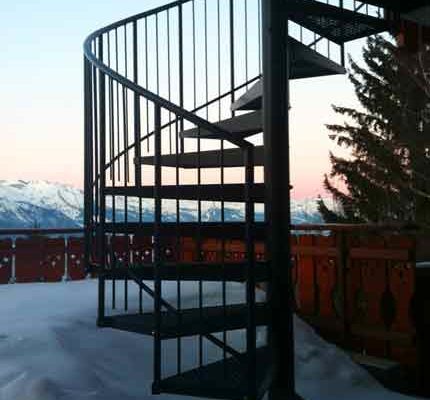 black outdoor spiral staircase with mountains to rear