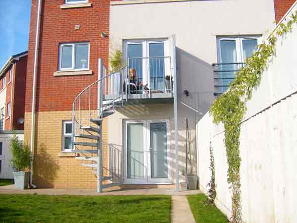 lady on top of an outdoor balcony to back of house with spiral staircase