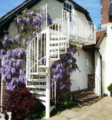 white outdoor spiral staircase with balcony with purple flowers