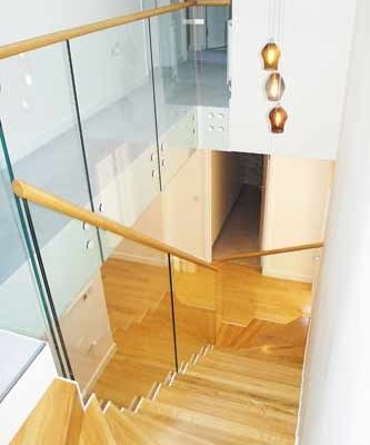 looking down an oak step stair with glass balustrade