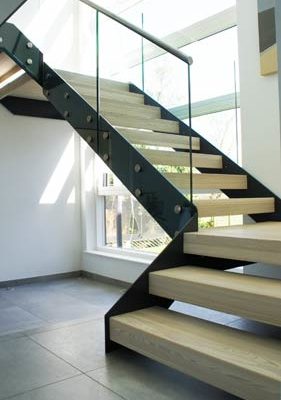 large black steel stringer stair with light timber steps and frameless glass
