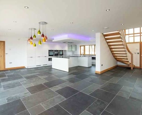 large grey tiled living area with kitchen and modern stair on show