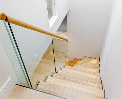 looking down a oak staircase with frameless glass balustrade