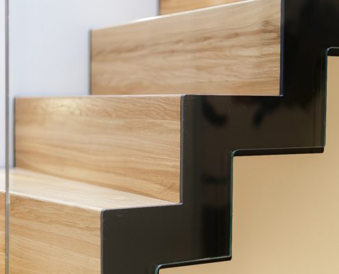 close up of black steel stringer with glass balustrade and wood treads