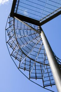 underside of grated steep spiral stair with blue sky beyond