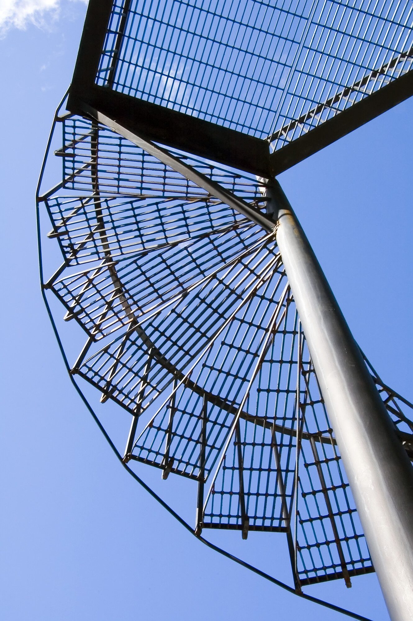 underside of grated steep spiral stair with blue sky beyond